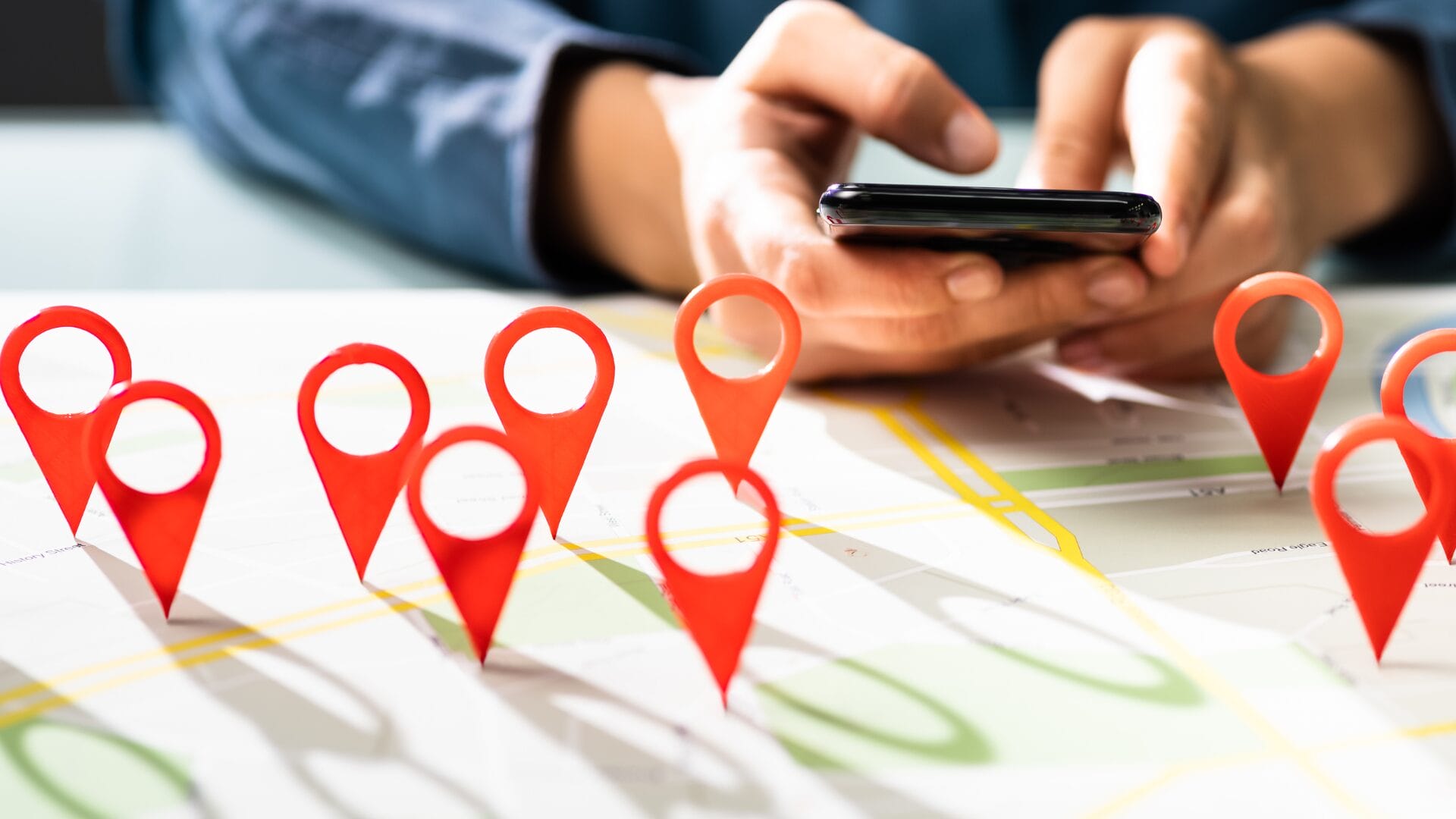 Close-up of a person using a smartphone over a map with red location pins, symbolizing the importance of balancing global reach and local relevance in multinational marketing campaigns