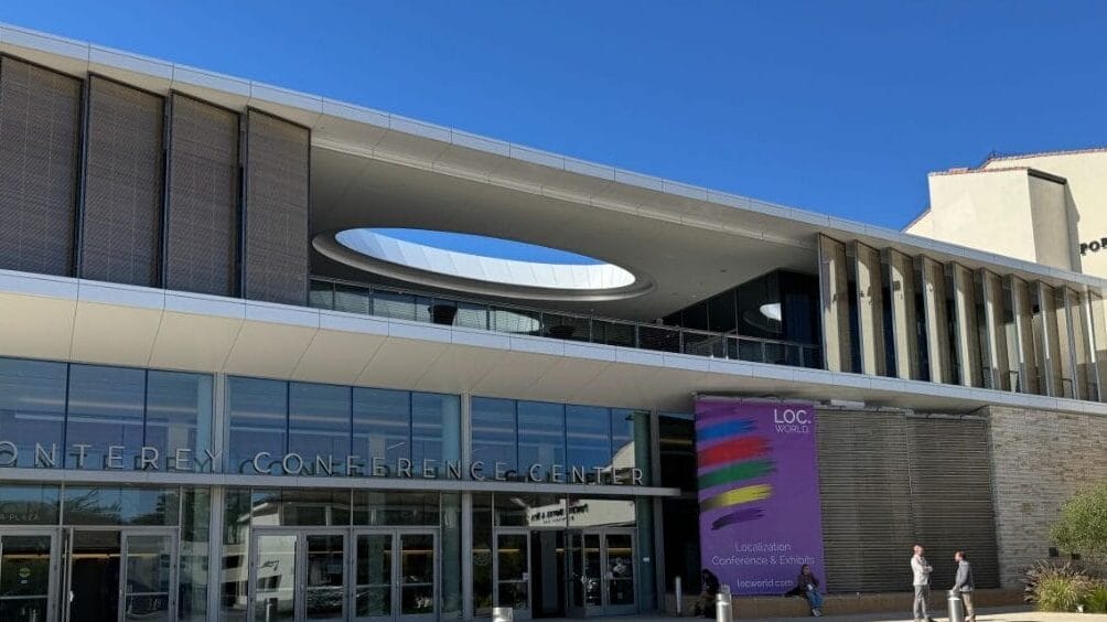 The exterior of the Monterey Conference Center with signage for LocWorld Monterey 2024, a conference focused on localization, AI, and global communication strategies, showing people entering the building under a clear blue sky.