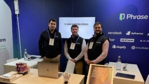 The Phrase Localization platform team at LocWorld 51 in Dublin, standing in front of their booth with a blue backdrop featuring logos of partner companies like Zendesk, Deliveroo, Decathlon, Shopify, and Snowflake. The team members are wearing black vests with the Phrase logo and name tags