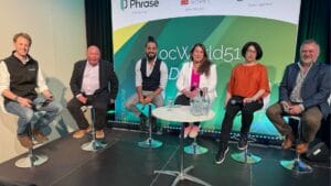 A panel of six people, including Georg Ell, CEO of Phrase, engaged in a discussion at LocWorld51. The panelists are seated on high stools in front of a backdrop displaying event sponsors. They are holding microphones and appear to be actively participating in the conversation.